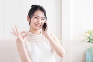 スマホで電話をしながらOKサインをする女性